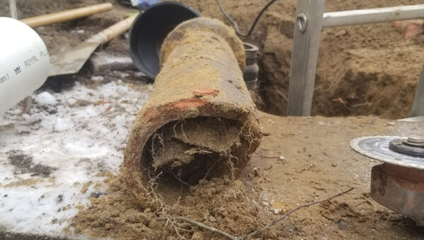 Close-up of a broken, dirt-covered pipe clogged with roots, lying on a concrete surface at an outdoor construction site. Tools, soil, and a ladder are visible in the background—typical scene for a plumber Toronto might handle.