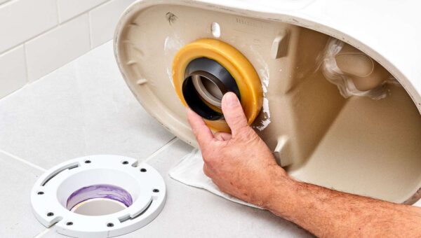 A plumber Toronto is installing a wax ring onto the bottom of a toilet, preparing it for placement over a floor flange on a tiled bathroom floor.