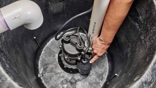 A person's hand adjusting a float switch on a sump pump inside a black plastic sump basin with attached pipes, as a plumber Toronto expert would do to ensure proper function.