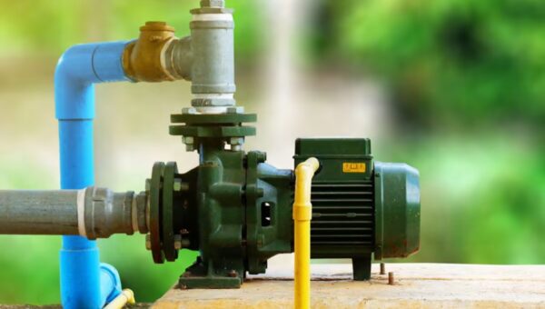 A green electric water pump is connected to blue and yellow pipes, mounted on a concrete surface, with a blurred green background, similar to setups installed by a skilled plumber Toronto residents trust.